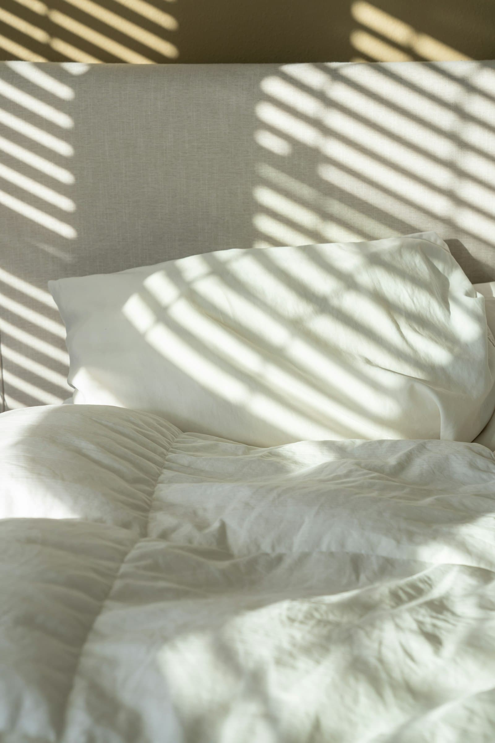 Morning light falling across freshly made white bed linen in a quiet bedroom